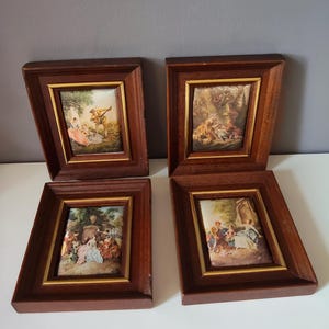 Può includere: Quattro piccoli dipinti incorniciati raffiguranti scene di persone in un giardino. Le cornici sono in legno scuro con un bordo interno dorato. I dipinti mostrano figure con abiti colorati.
