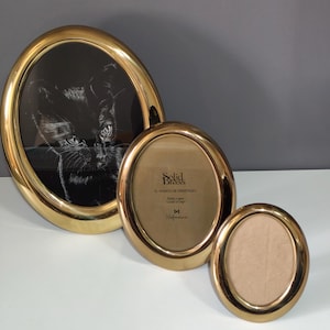 Peut inclure: Trois cadres ovales en laiton de différentes tailles. Le plus grand cadre contient une image en noir et blanc d'un chat. Le cadre du milieu porte l'inscription "Solid Brass". Le plus petit cadre est vide.