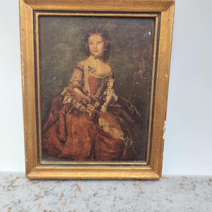 Pode incluir: Retrato emoldurado de uma pessoa jovem em um vestido vermelho com acabamento em renda, segurando flores. A pintura tem uma moldura dourada e está sobre um fundo verde escuro. A obra de arte parece ser antiga.
