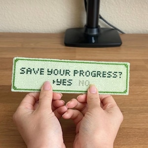 Può includere: Un segnalibro a punto croce verde e bianco con il testo "SAVE YOUR PROGRESS? YES NO".