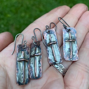 Puede incluir: Un par de pendientes de plata y cobre con textura martillada y dise&ntilde;o de cruz.