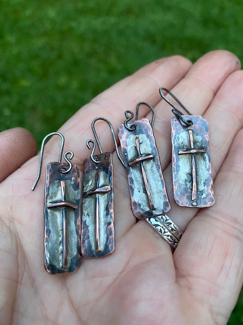 Puede incluir: Un par de pendientes de plata y cobre con textura martillada y dise&ntilde;o de cruz.