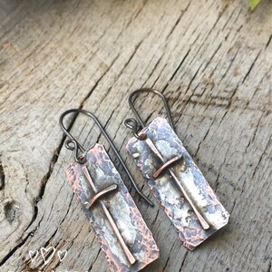 Puede incluir: Un par de pendientes de cobre martillado con un dise&ntilde;o de cruz. Los pendientes son de color plateado y cobre y tienen un aspecto r&uacute;stico.