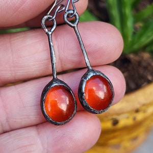May include: A pair of dangle earrings with orange glass cabochons set in silver metal.