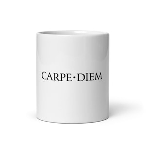 Puede incluir: Una taza de cerámica blanca con el texto CARPE DIEM impreso en una fuente serif negra en el centro. La taza tiene un cuerpo cilíndrico liso con un acabado limpio, mostrando las letras negras en contraste con la superficie blanca.