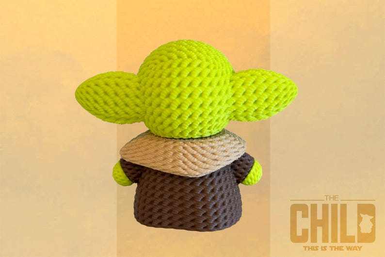 May include: A handmade green and brown crocheted figure of The Child, with large ears and a brown robe. The figure is made of textured yarn and has a tan collar. The text "THE CHILD" and "THIS IS THE WAY" is visible.