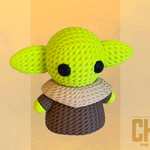 May include: A crocheted figure of The Child, featuring a lime green head with large ears and black eyes. It wears a tan and brown outfit. The text "THE CHILD THIS IS THE WAY" is in the lower right corner.