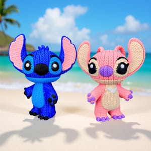 May include: Two character figurines, one blue and one pink, stand side-by-side on a sandy beach. The blue figure has large ears with pink accents, while the pink figure has similar features. Both have large eyes and are in a standing pose.