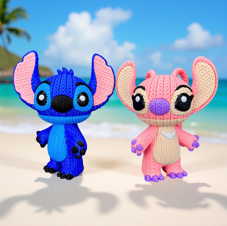 May include: Two character figurines, one blue and one pink, stand side-by-side on a sandy beach. The blue figure has large ears with pink accents, while the pink figure has similar features. Both have large eyes and are in a standing pose.