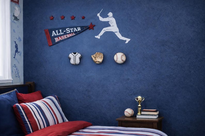 May include: A blue wall featuring a baseball-themed wall decal set with a white silhouette of a batter, a blue pennant with the text ALL-STAR BASEBALL, and three wall-mounted decor pieces shaped like a jersey, a baseball glove, and a baseball.