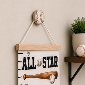 May include: A white canvas growth chart hanging from a baseball-shaped wooden knob with a white rope. The chart features the text ALL STAR, a wooden baseball bat, a baseball, and a red and white baseball jersey with measurement markings.
