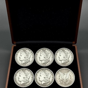 Puede incluir: Una taza de cerámica blanca con un asa negra y el texto "But First, Coffee" en negro, con una fuente de estilo manuscrito. La taza está sobre una superficie blanca.