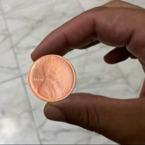 May include: A copper-colored penny coin from 1969, held between fingers. The coin features a profile of Abraham Lincoln and the word "LIBERTY". The words "IN GOD WE TRUST" are visible at the top.