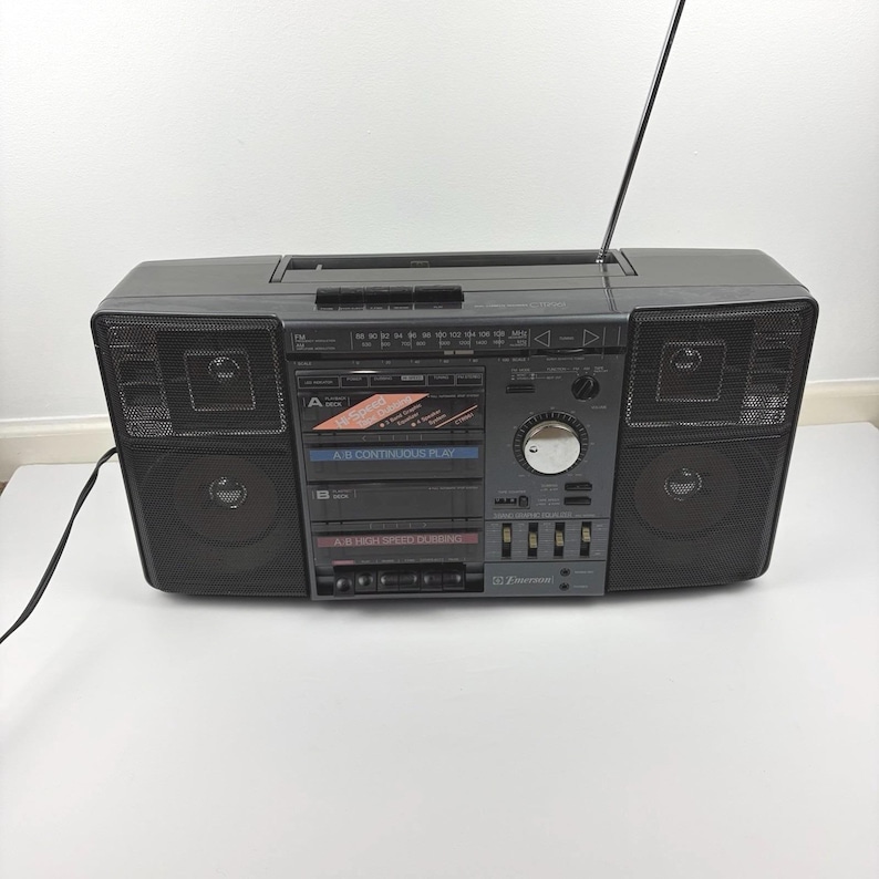 May include: A vintage gray boombox with a retractable antenna, speakers on each side, and a central control panel. The boombox features a cassette player and radio controls. The text "A-B CONTINUOUS PLAY" is visible.