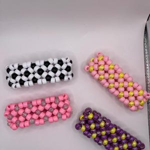 May include: Four colorful beaded bracelets, each with a different pattern. The bracelets are made with black and white beads, pink and white beads, yellow and pink beads, and purple and yellow beads.