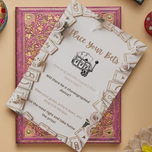 May include: A wedding game card with the text "Place your Bets" and questions about the couple's first dance. The card features a slot machine graphic and is decorated with floral accents and dice.