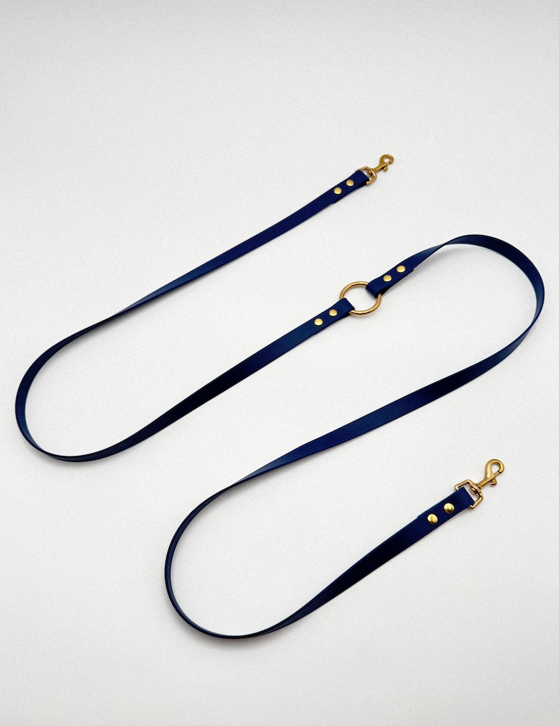 May include: A navy blue leather dog leash with gold hardware and a ring in the middle. The leash is on a white background.