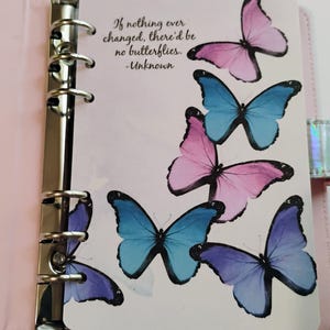 May include: A light pink binder with a metal six-ring mechanism featuring a white page printed with blue, purple, and pink butterflies and the text: If nothing ever changed, there'd be no butterflies. -Unknown. The binder has a holographic closure.