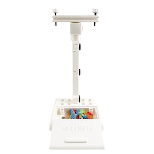 May include: A white Miraneks embroidery stand with a rectangular base and adjustable height. The stand has a storage compartment containing colorful embroidery floss. The text "MIRANEKS" is printed on the front.