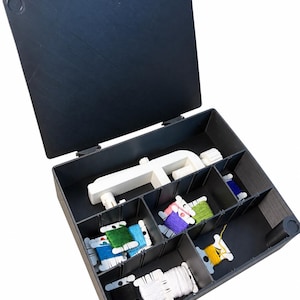 May include: A black plastic storage box with an open lid, featuring multiple compartments containing various colorful embroidery floss bobbins and a white plastic thread winder tool. The interior is divided into sections to organize the supplies.