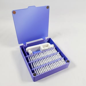 May include: A purple plastic organizer box with a hinged lid, open to reveal a white clamp and numerous small white packets. The box has a rectangular shape with rounded corners and is set against a white background.