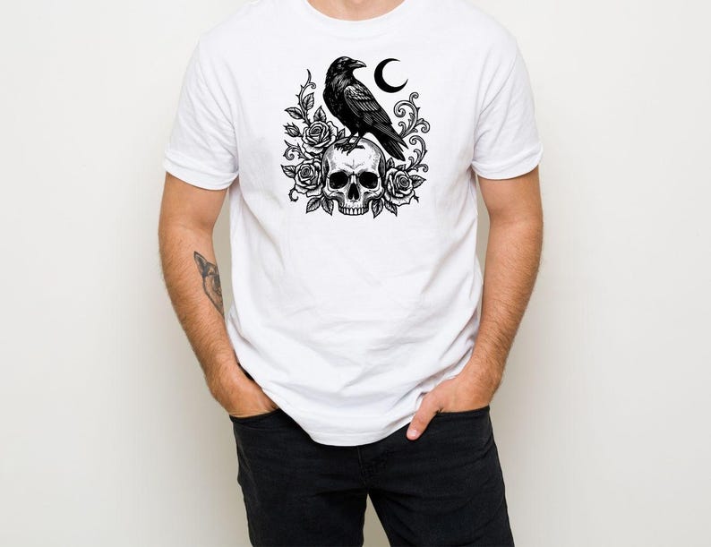 Puede incluir: Una camiseta blanca de manga corta con un estampado gr&aacute;fico negro en el pecho. El dise&ntilde;o muestra un cuervo posado sobre un cr&aacute;neo humano, rodeado de rosas en flor, enredaderas espinosas y una luna creciente en una ilustraci&oacute;n detallada.