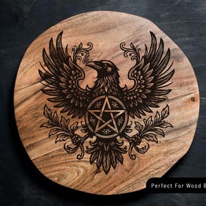 Puede incluir: Una tabla de madera redonda con veta natural que presenta un dise&ntilde;o grabado con l&aacute;ser en negro de un cuervo con las alas extendidas, sosteniendo un s&iacute;mbolo de pentagrama rodeado de ramas decorativas. El texto Perfect For Wood Burning es visible.