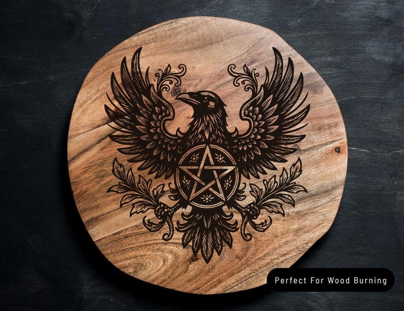 Puede incluir: Una tabla de madera redonda con veta natural que presenta un dise&ntilde;o grabado con l&aacute;ser en negro de un cuervo con las alas extendidas, sosteniendo un s&iacute;mbolo de pentagrama rodeado de ramas decorativas. El texto Perfect For Wood Burning es visible.