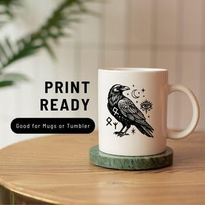 Puede incluir: Una taza de cer&aacute;mica blanca con una ilustraci&oacute;n gr&aacute;fica negra de un cuervo rodeado de s&iacute;mbolos celestiales, incluyendo una luna creciente, estrellas y un ojo. El texto PRINT READY y Good for Mugs or Tumbler aparece a la izquierda de la taza.