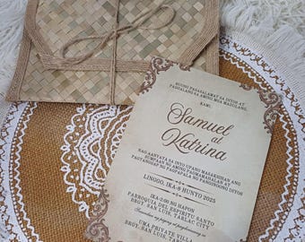 Puede incluir: Un sobre tejido con una atadura de cuerda descansa sobre un mantel individual de arpillera con un diseño de encaje blanco. Una invitación de boda con bordes ornamentados y texto también está en el mantel individual. La invitación dice "Samuel at Katrina".