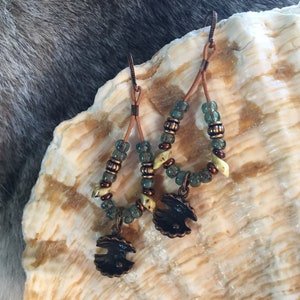 May include: A pair of dangle earrings with copper wire, green and white beads, and a copper charm in the shape of a bird.