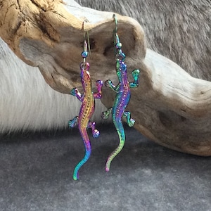 May include: A pair of iridescent rainbow lizard earrings. The earrings are made of metal and have a detailed lizard design. The lizards are facing opposite directions.