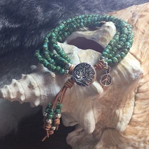 May include: A turquoise beaded bracelet with a silver tree of life charm and a peace sign charm. The bracelet is layered and has a brown leather tassel.