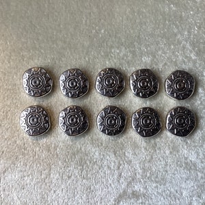 May include: Ten silver-toned buttons with a geometric design. Each button features a circular pattern with a starburst design.