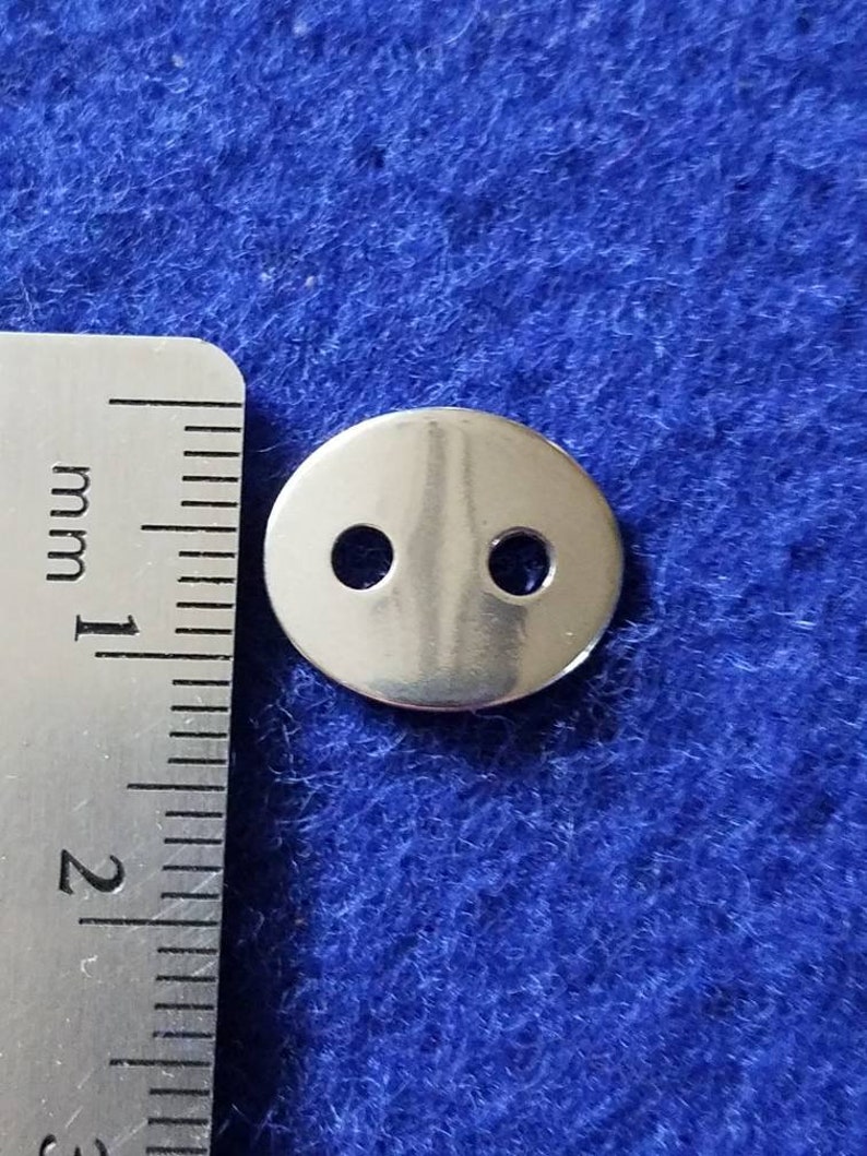 May include: A silver metal button with two holes. The button is approximately 1 cm in diameter.