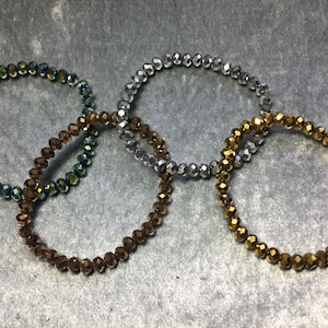 May include: Three beaded bracelets in silver, gold, and blue-green colors. The bracelets are made of faceted glass beads.