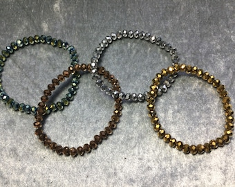May include: Three beaded bracelets in silver, gold, and blue-green colors. The bracelets are made of faceted glass beads.
