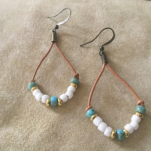 May include: A pair of dangle earrings with brown leather cords and turquoise and white beads.