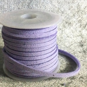 May include: A spool of lavender purple suede cord, wound around a clear plastic spool. The cord is about 1/4 inch wide and has a slightly textured surface.