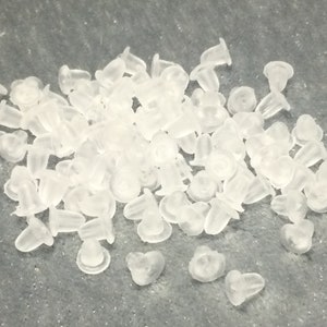 May include: A large pile of clear plastic earring backs. The backs are small and round with a small hole in the center.