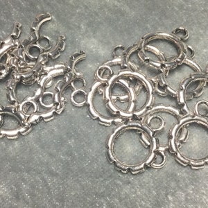 May include: A pile of silver-toned metal jump rings with a decorative scalloped edge. The rings have a small loop on the top for attaching to jewelry or other crafts.