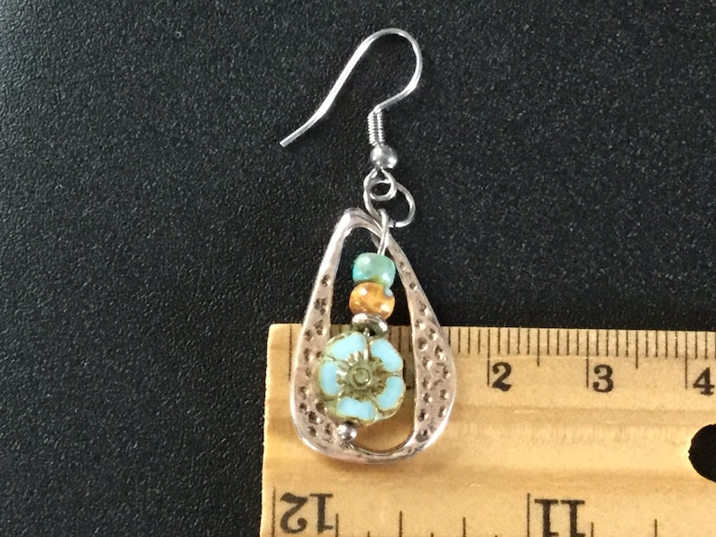 May include: Silver dangle earrings with a teardrop-shaped design. The earrings feature a blue and white flower bead, orange and green beads, and a silver hook.