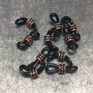 May include: Eight black metal cord ends with copper accents. Each end has a loop on each side and a copper bead in the center.