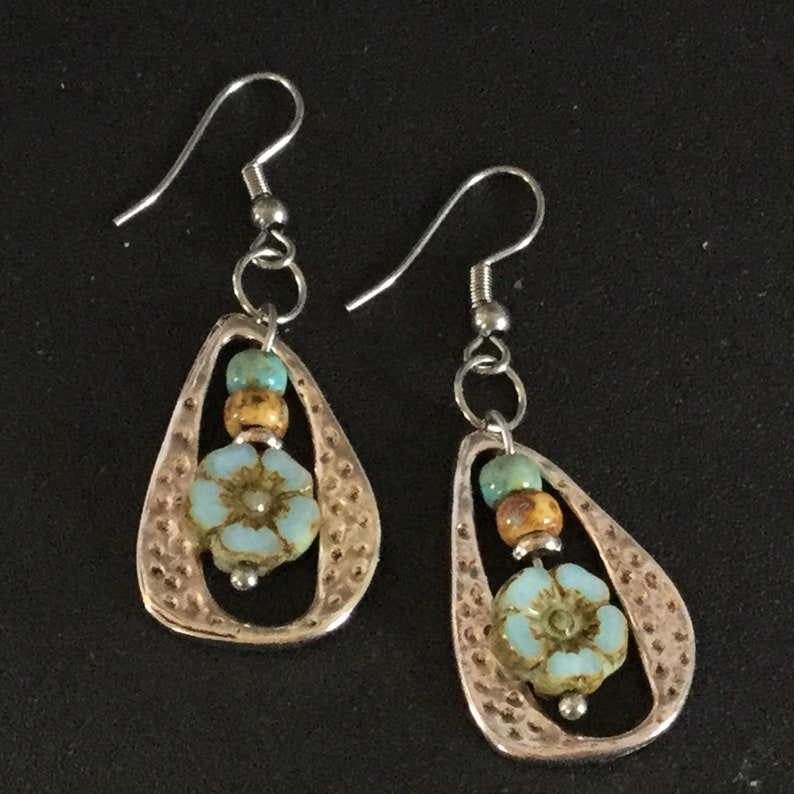 May include: Silver dangle earrings with a teardrop shaped metal frame, a blue and brown bead, and a blue flower charm.