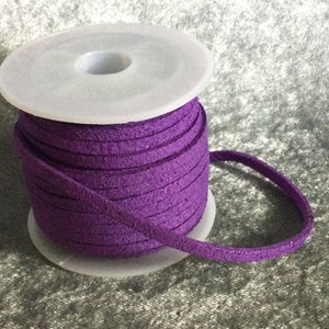 May include: A spool of purple suede cord, wound around a white plastic spool. The cord is approximately 3 mm wide.
