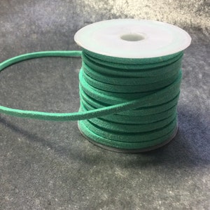 May include: A spool of light green suede cord. The cord is wound around a white plastic spool.