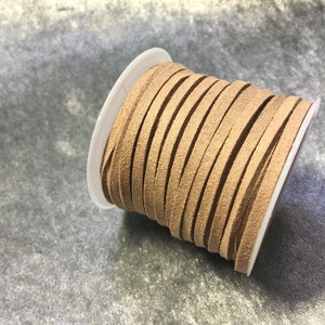 May include: A spool of tan-colored suede leather cord. The cord is tightly wound on a white plastic spool. The suede appears soft and has a slightly textured surface. Ideal for crafting and jewelry making.