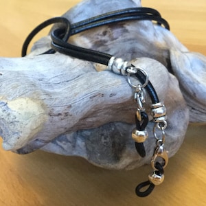 May include: Black leather eyeglass chain with silver beads and a silver clasp. The chain is looped over a piece of driftwood.