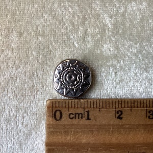 May include: A silver-toned button with a decorative design featuring a sun and moon motif. The button is approximately 1 cm in diameter.