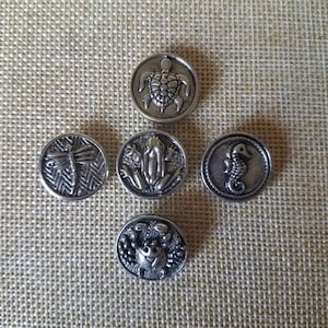 May include: Five silver-toned metal buttons with different animal designs. The buttons feature a turtle, a frog, a dragonfly, a seahorse, and a crab.